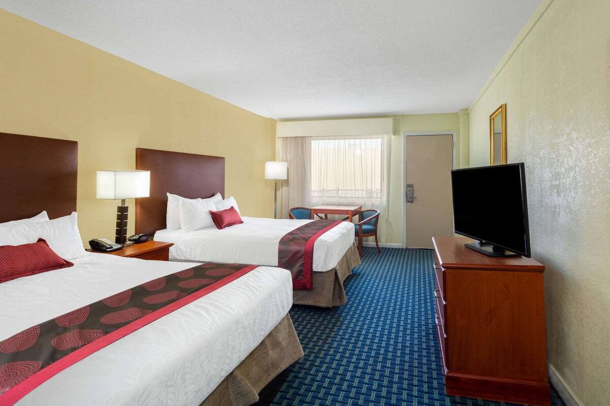 A hotel room with two beds, a desk, a chair, a television, and a window with curtains.
