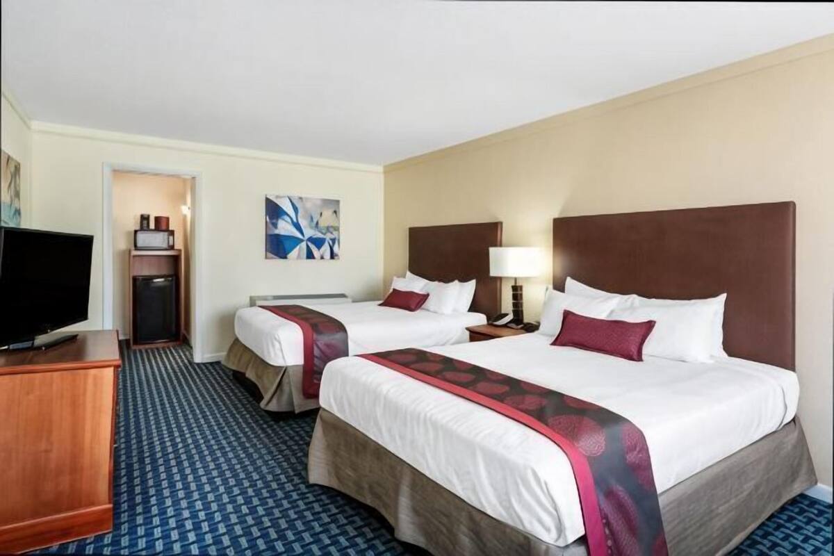 A hotel room with two beds, a TV, a desk, and a painting on the wall.