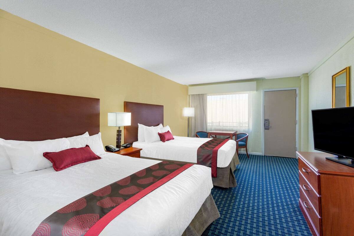 A hotel room with two beds, a desk, a television, and a bathroom door.