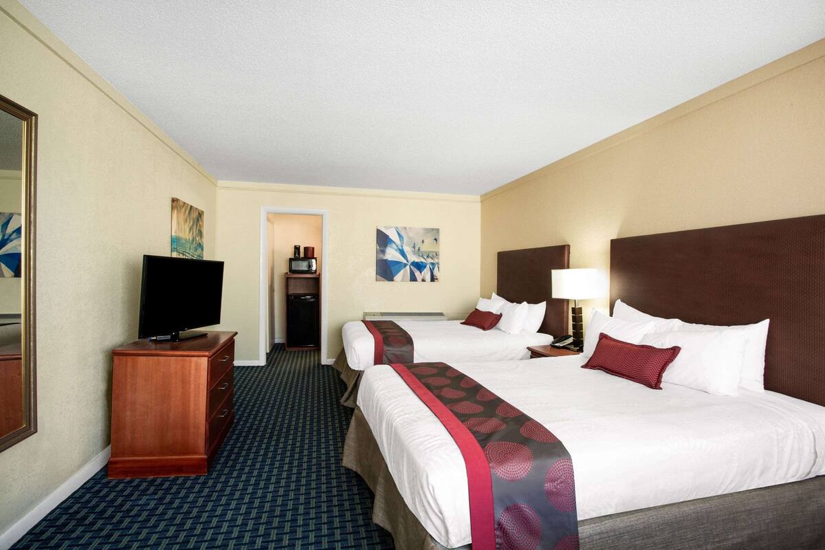 A hotel room with two beds, a television, a dresser, and artwork on the walls.