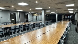 Un salón de conferencias con una larga mesa de madera rodeada de sillas, suelo alfombrado e iluminación empotrada en el techo.