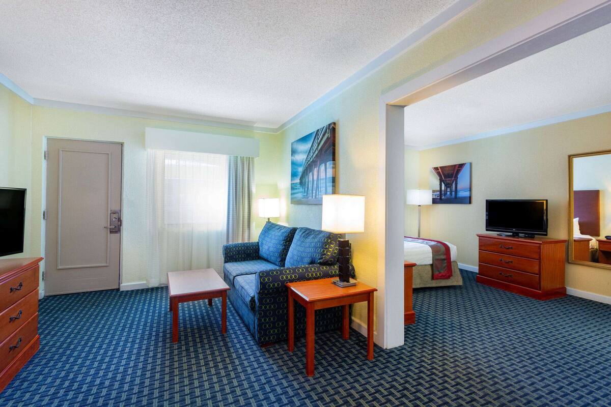 A hotel room with a sofa, two lamps, a TV, a dresser, and a mirror.