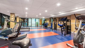 Un gimnasio con máquinas de cardio, equipo de levantamiento de pesas y suelo azul y naranja.