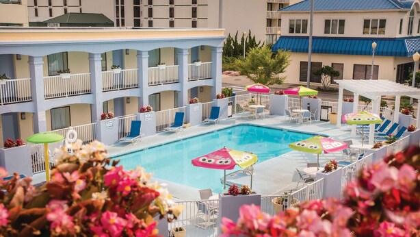 Zona de piscina de hotel con varios niveles de balcones, mobiliario exterior y sombrillas.