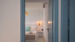Un couloir étroit mène à une chambre à coucher équipée d’un lit, d’une table de chevet et d’un luminaire fixé au mur.