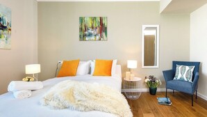 Une chambre d’hôtel avec un lit, une chaise, un tableau, un miroir et une table de chevet avec une lampe.