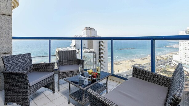 Un balcon agrémenté de meubles en osier, d’une table en verre et offrant une vue sur la plage et l’océan.