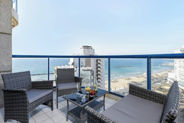 A balcony with wicker furniture, a glass table, and a view of the beach and ocean.