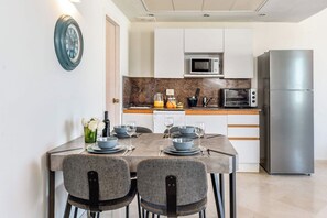A modern kitchen with a dining table set for two, a microwave, a toaster oven, and a stainless steel refrigerator.