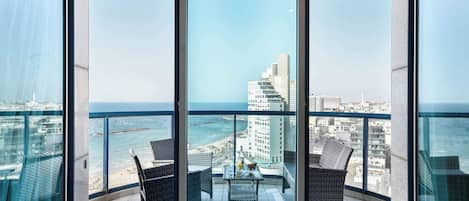 A balcony with two wicker chairs and a table, overlooking a cityscape and the sea.