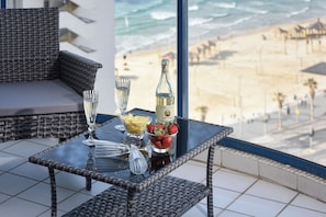 A balcony with wicker furniture, a glass table, and a bottle of champagne.