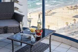 A balcony with wicker furniture, a glass table, a bottle of champagne, and a bowl of strawberries.