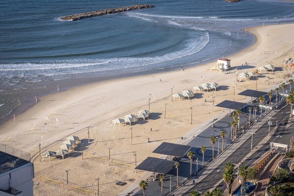 A beach with a road, beach umbrellas, and a lifeguard tower.