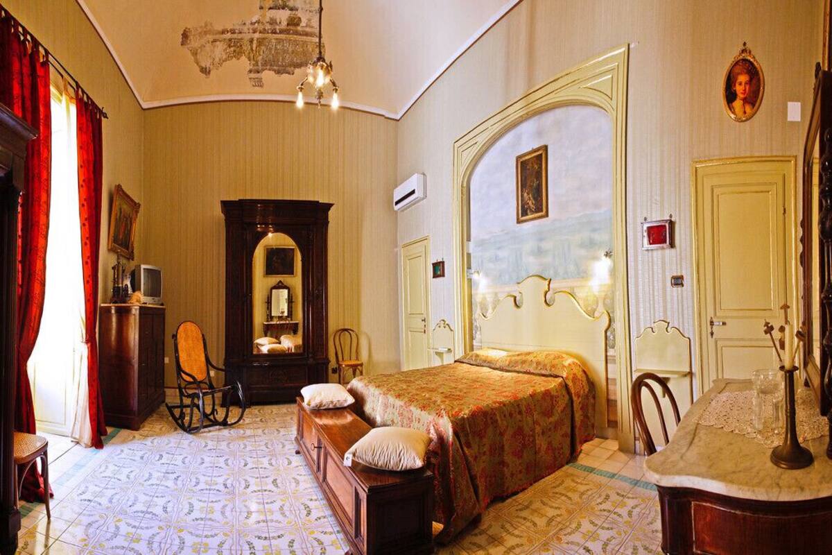 A classic hotel room with a large bed, a wooden wardrobe, a desk with a chair, and a mirror.