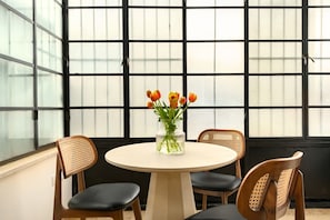 A room with a round table, two chairs, and a vase with flowers.