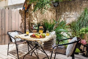 Eine Terrasse im Freien mit einem Holztisch, gedeckt für zwei Personen, umgeben von Korbstühlen.