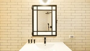 A bathroom with a white sink, a mirror with a black frame, and a shower visible in the reflection. - Chic 1BR Apt Featuring Urban Design in the City (Tel Aviv-Yafo)