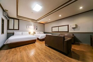 A hotel room with two beds, a sofa, wooden flooring, and a ceiling with recessed lighting. - Sharp Hotel (Andong)
