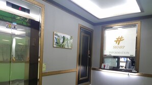 Un ascensor con pantalla digital, una puerta y una pared con un cuadro enmarcado y un letrero que dice "SHARP INFORMATION".