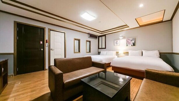 Habitación de hotel con dos camas, un sofá, una mesa de centro y suelo de madera.