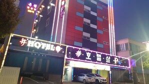 Un hotel con fachada moderna, señalización de neón y un estacionamiento con coches.