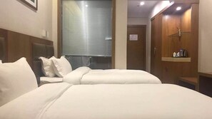 Une chambre d’hôtel avec deux lits, une armoire en bois et une petite étagère avec des articles de toilette.