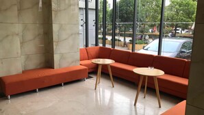 A modern interior with a curved orange sofa, two round wooden tables, and a large window offering a view of the street outside. - Vyluk J Hotel Fuxing Road Lijiang (Lijiang)