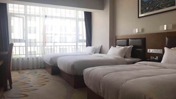 A hotel room with two beds, a large window with curtains, a headboard, and a framed picture on the wall. - Vyluk J Hotel Fuxing Road Lijiang (Lijiang)