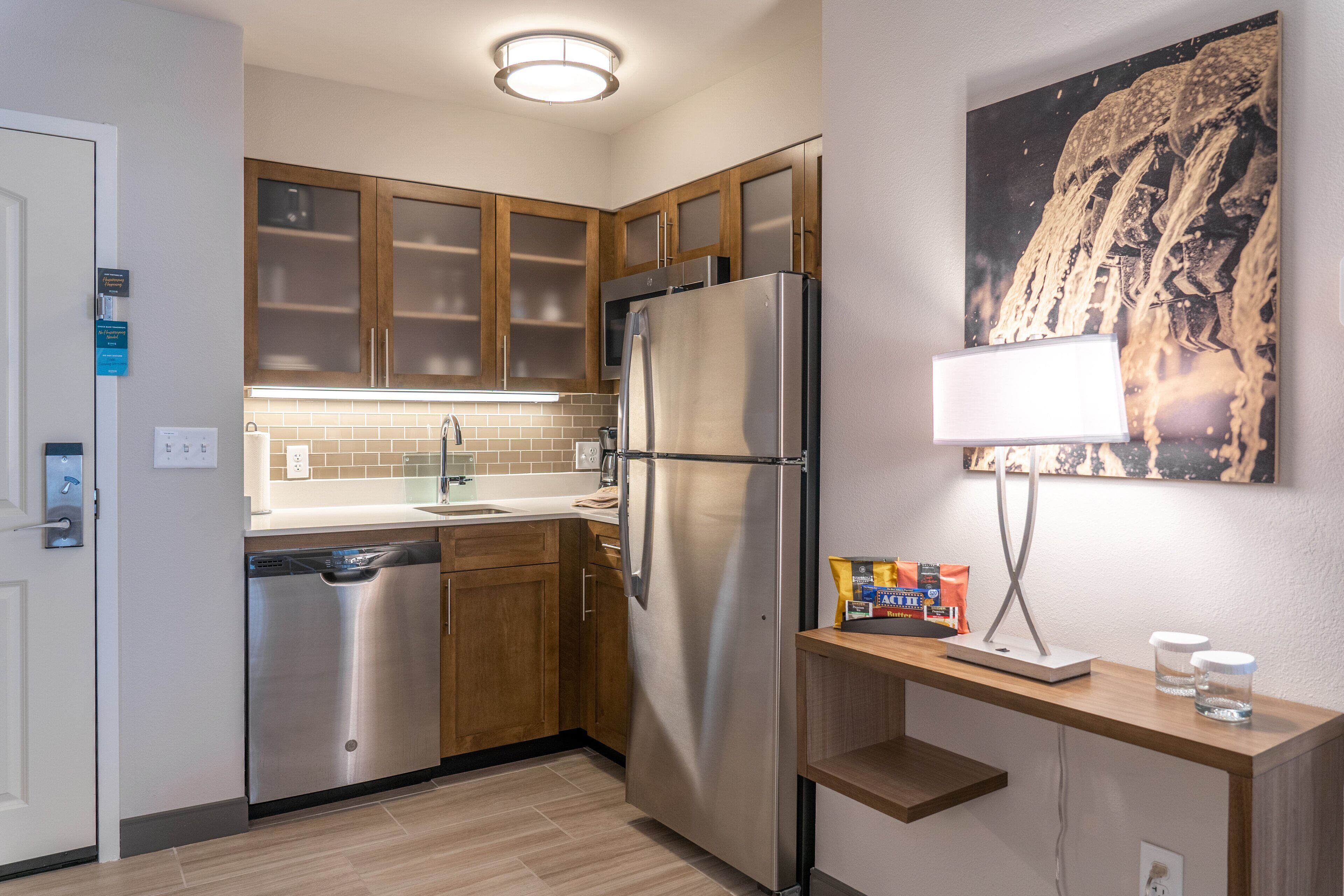 A modern kitchen with stainless steel appliances, wooden cabinets, a tiled backsplash, and a wall-mounted light fixture.