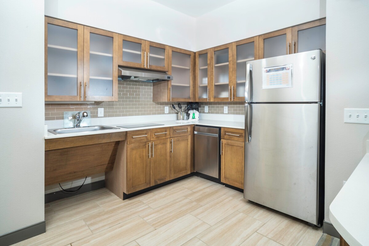 A modern kitchen with wooden cabinets, a stainless steel refrigerator, and a tiled backsplash.