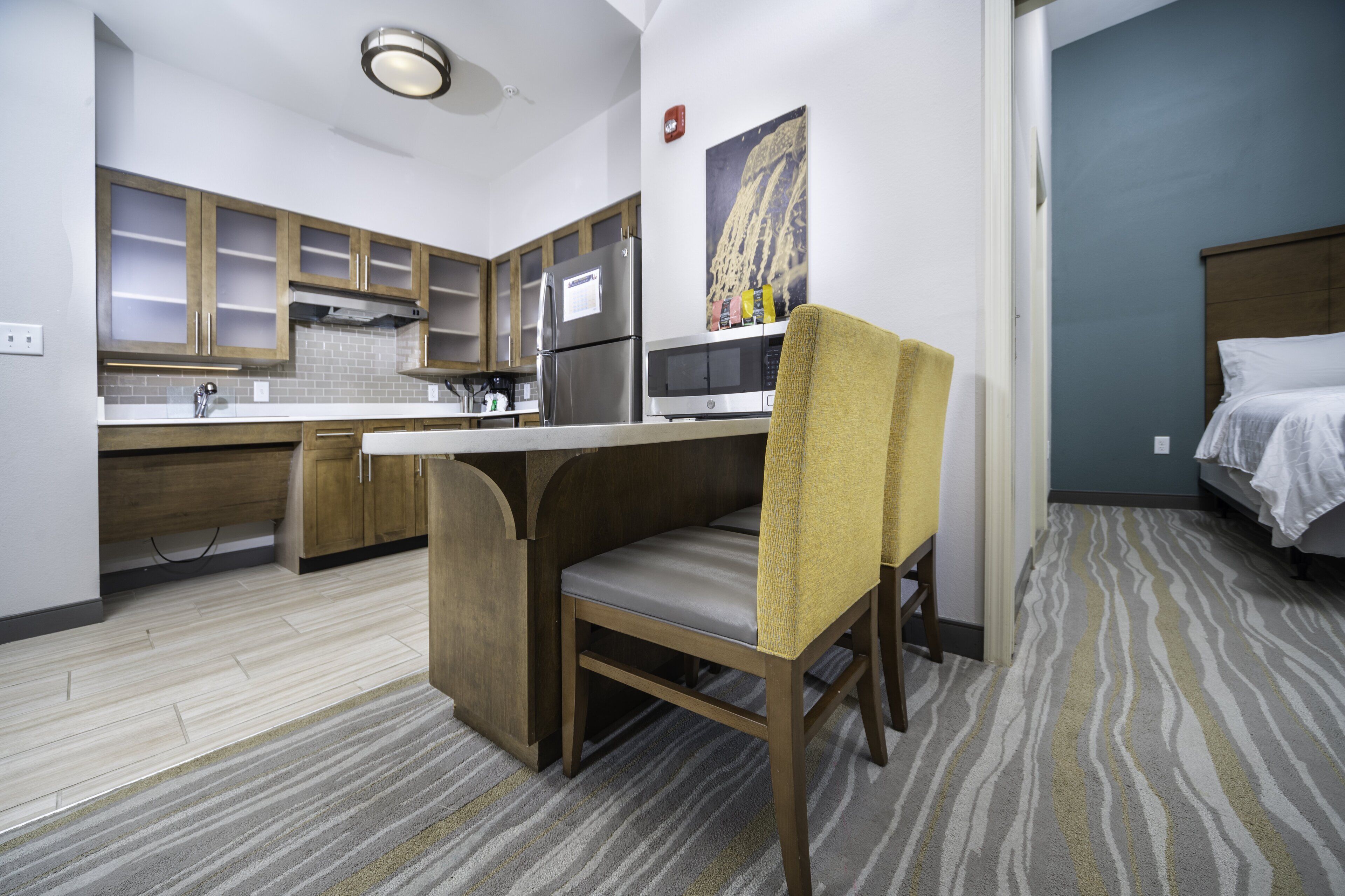 A compact kitchen with modern appliances, a dining area with a bench, and a bedroom with a bed.