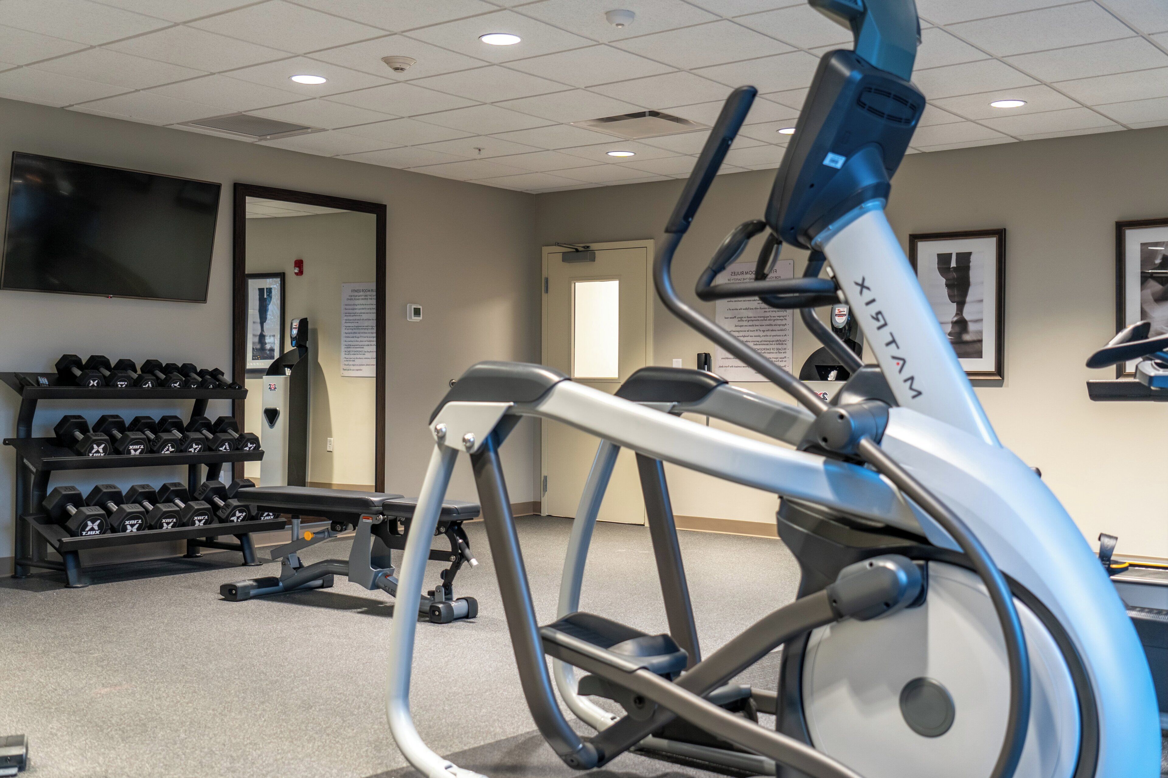 Un gimnasio con equipo de ejercicio, una televisión y un estante para mancuernas en la pared.
