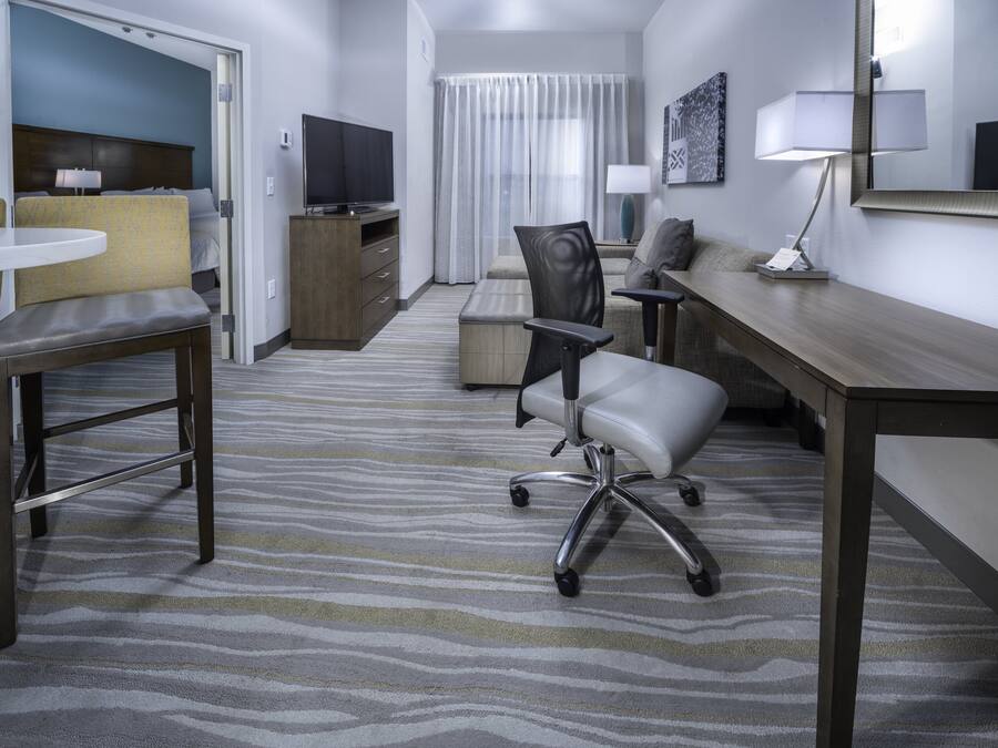 A hotel room with a bed, a desk, a chair, a television, a lamp, and a window with curtains.