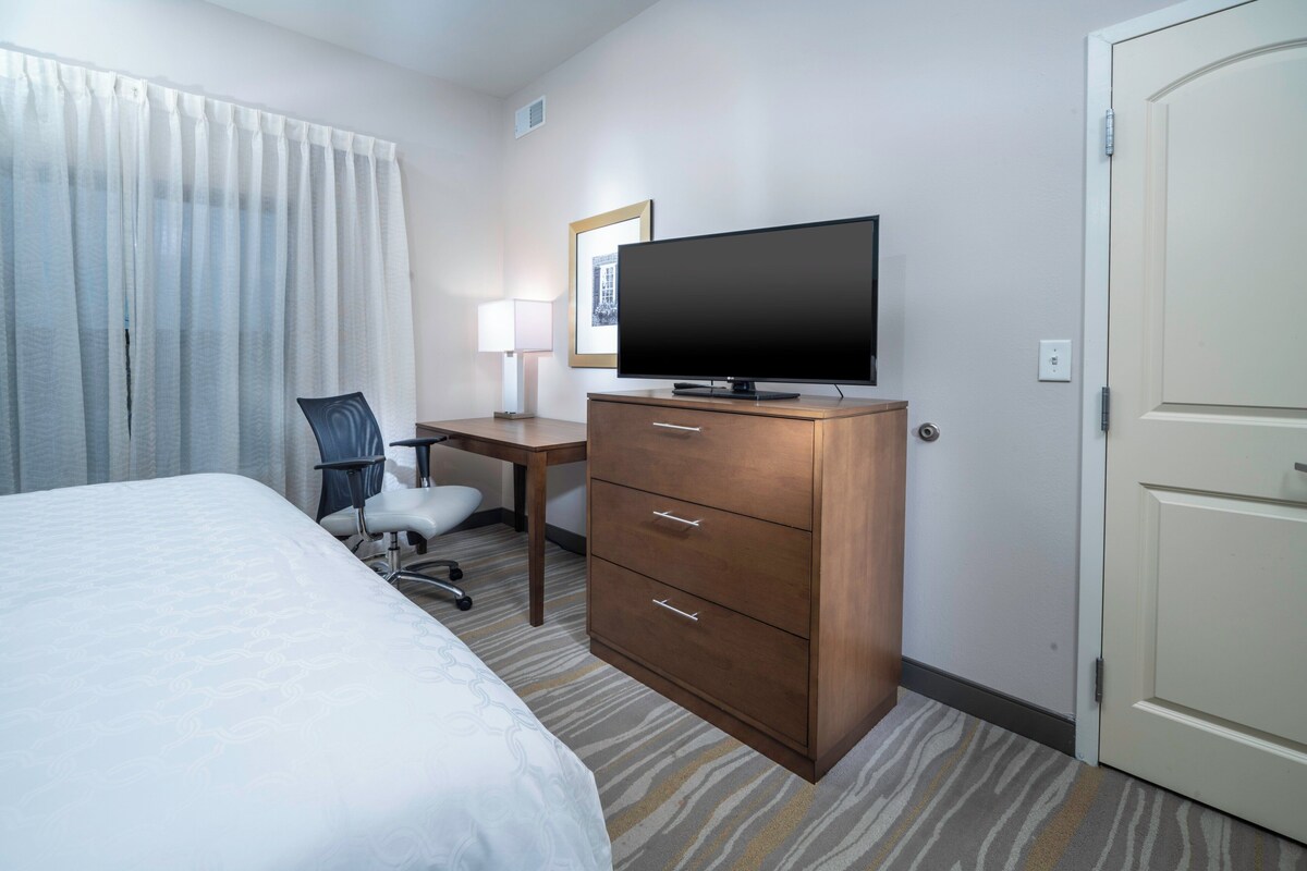 A hotel room with a bed, a desk with a chair, a television, and a wardrobe.