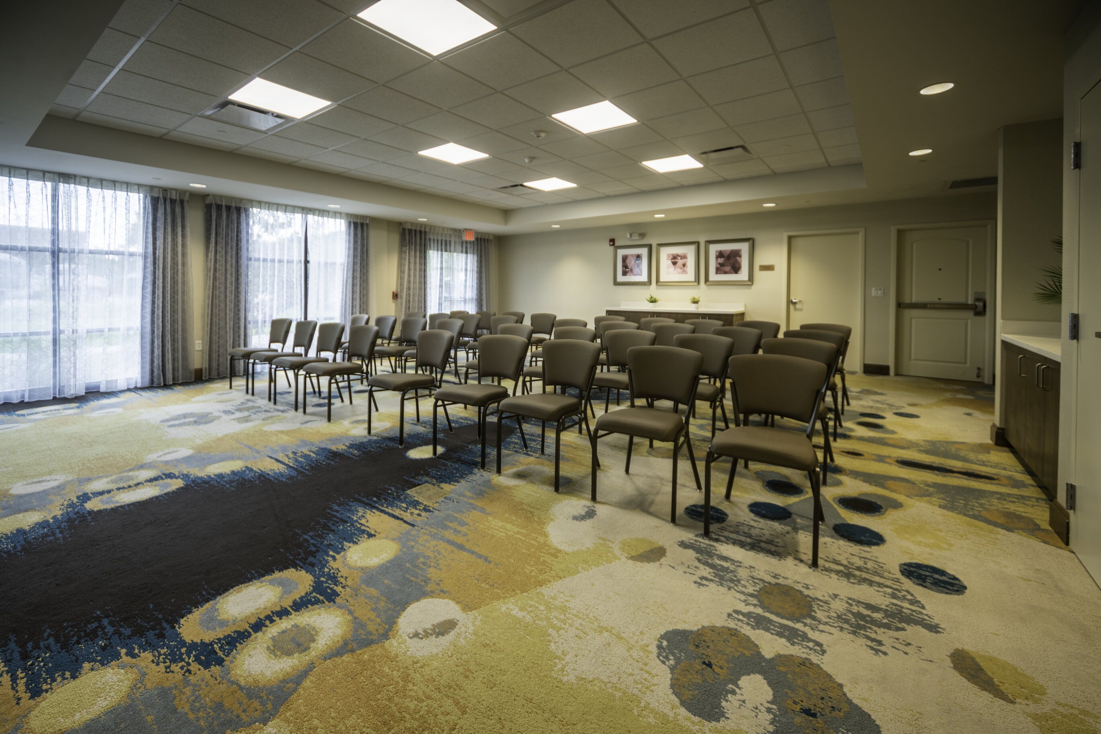 A conference room with rows of chairs, large windows, and a patterned carpet.