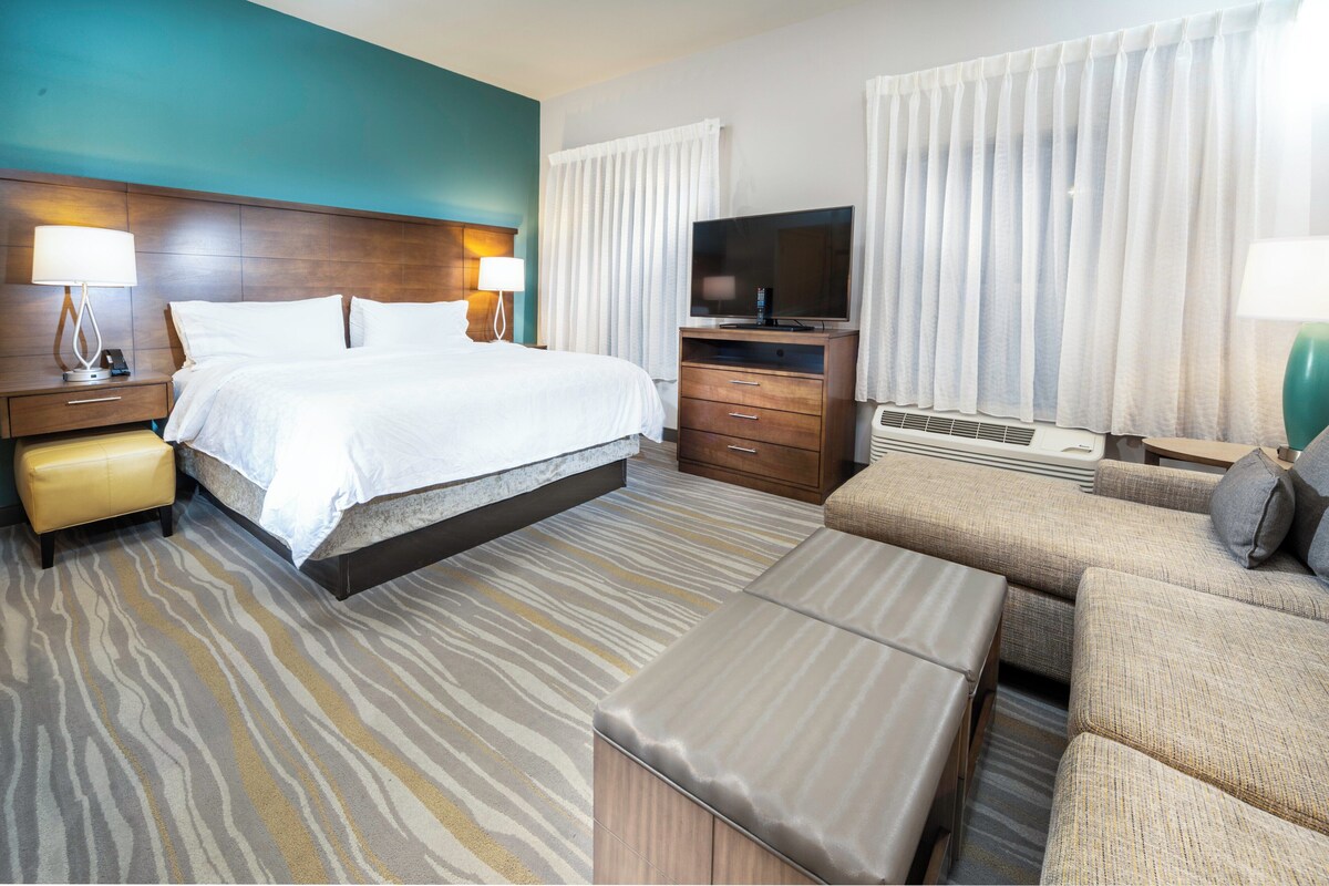 A hotel room with a bed, a TV, a sofa, and a desk with a lamp.