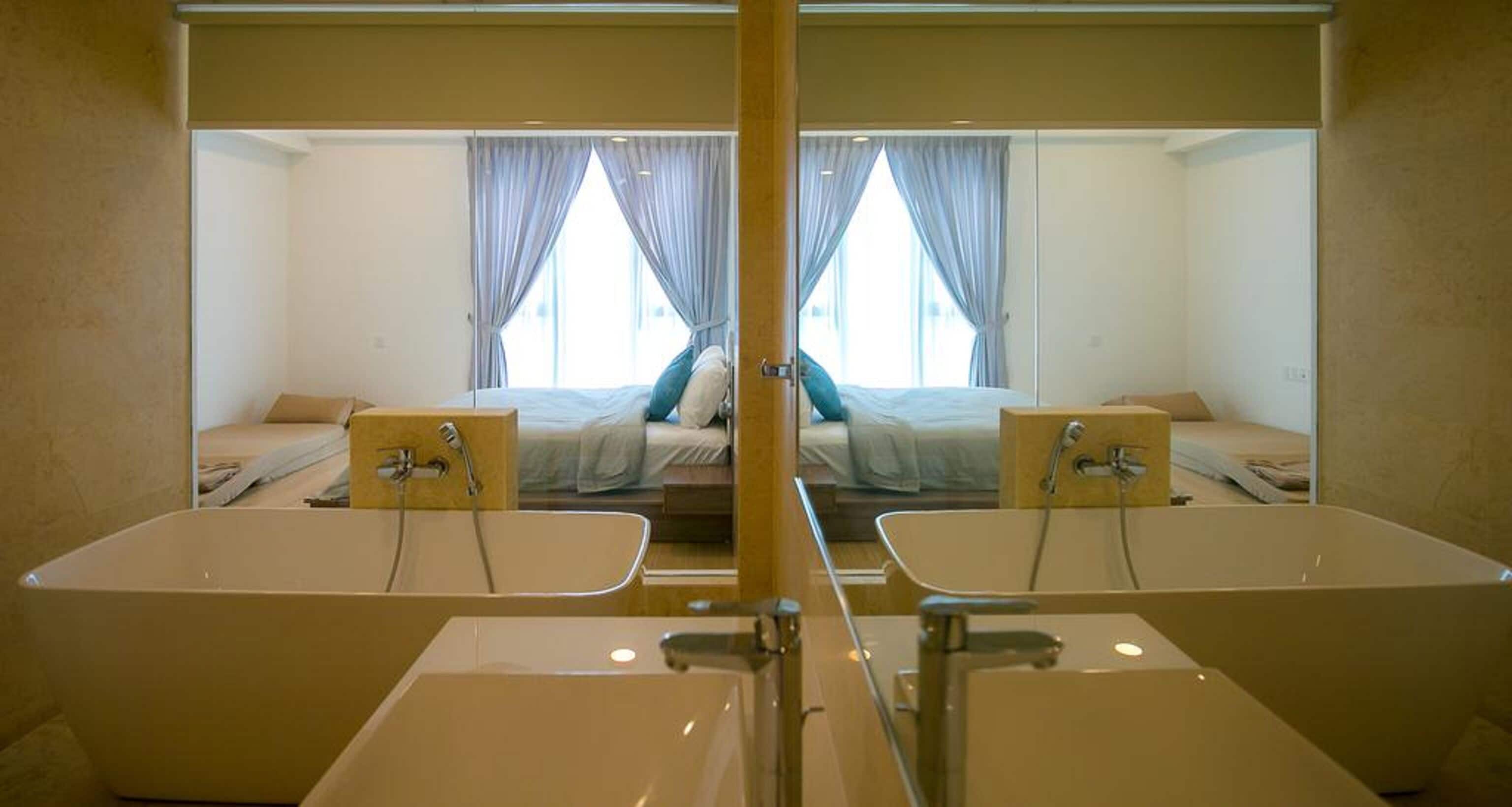 Une salle de bain aux murs recouverts de miroirs, avec deux lavabos, et un lit doté de rideaux.