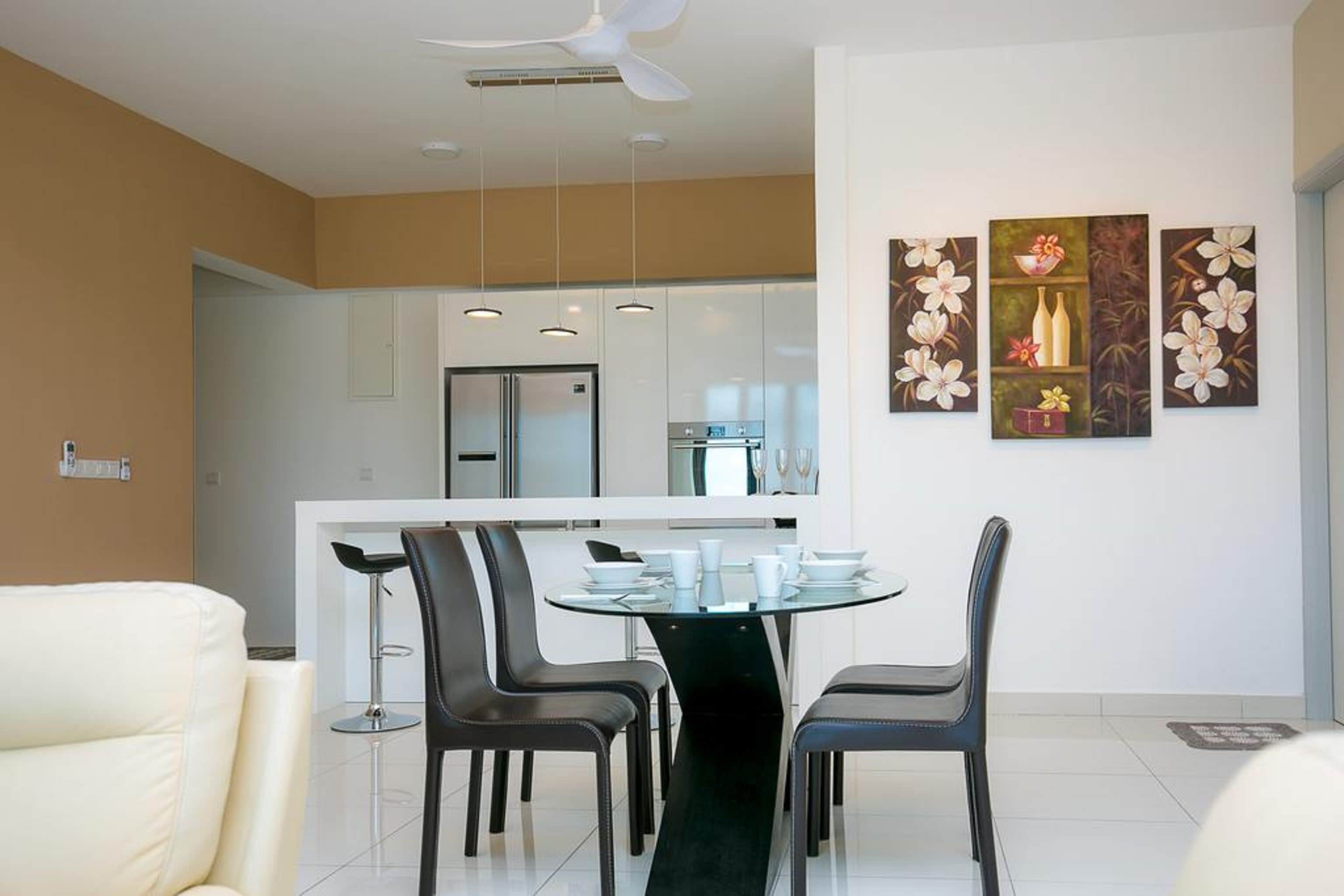 A modern dining area with a round glass table, black chairs, and a white ceiling fan.