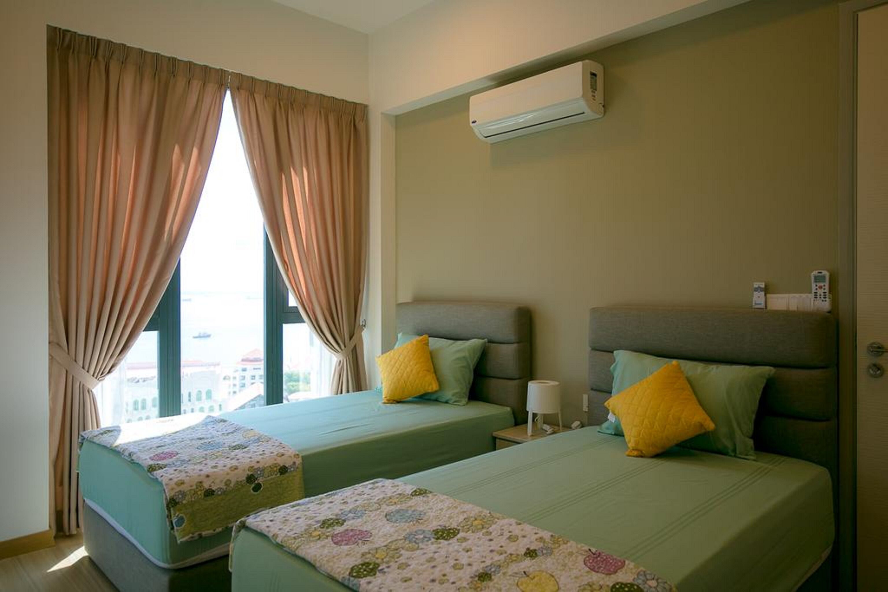A hotel room with two beds, beige curtains, an air conditioning unit, and a view of the city.