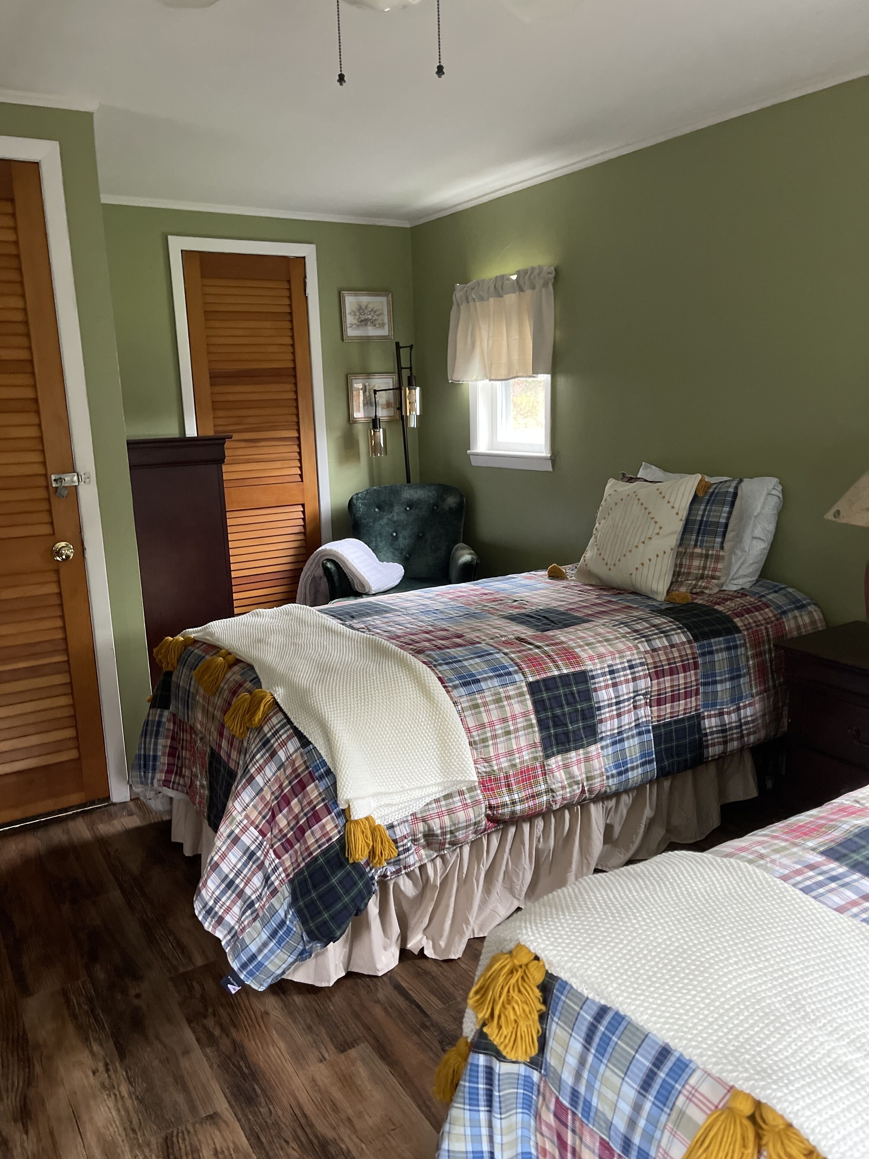 Un dormitorio con cama, una silla, un armario y ventana.