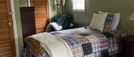 Un dormitorio con cama, una silla, un armario y ventana.