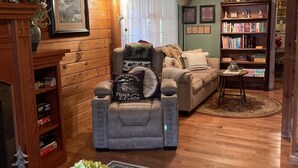 Una sala de estar acogedora de estilo cabaña con chimenea, un sofá, un sillón reclinable, una estantería y una mesa de centro con mantel a cuadros.