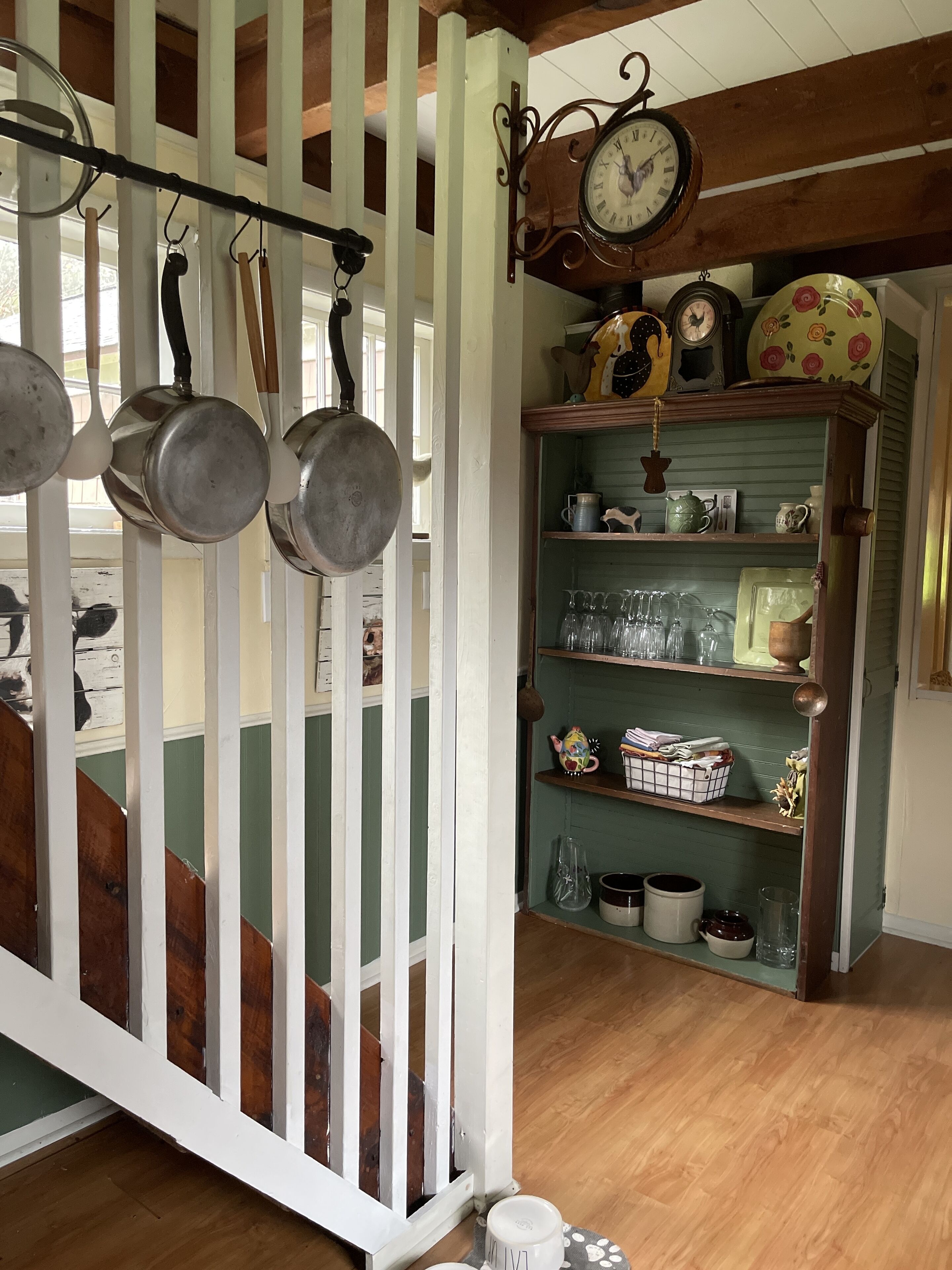 A kitchen with hanging pots, a clock, and shelves with various kitchenware.