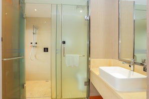 Un baño moderno con cabina de ducha de vidrio, lavamanos blanco y un espejo grande.
