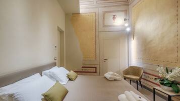 A hotel room with a bed, pillows, a chair, a table with towels, and a potted plant.