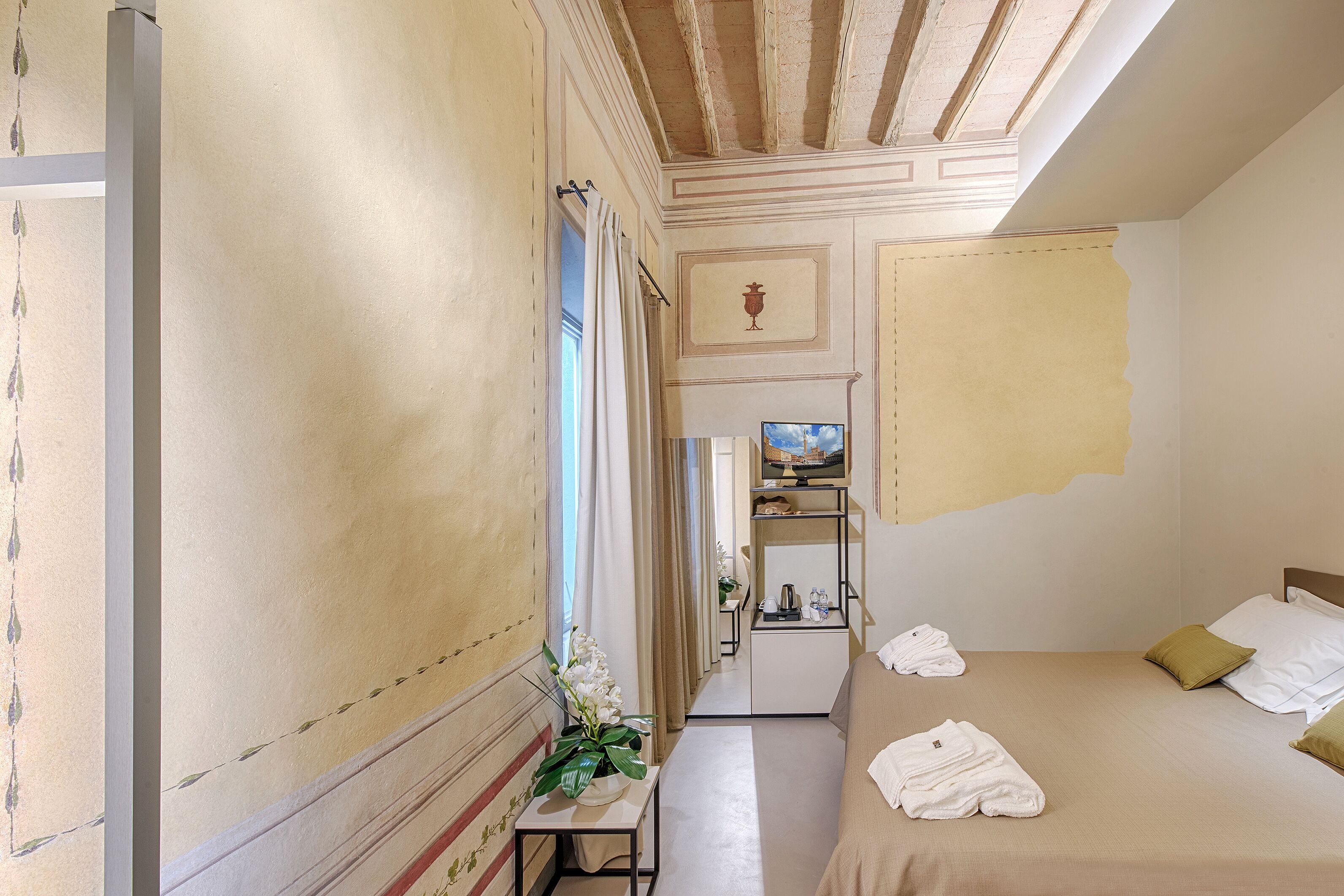 Una habitación de hotel con una cama, una mesita con una planta, un televisor y un minibar.