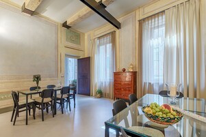 Zona pranzo con tavolo in vetro, sedie, una ciotola di frutta, un armadio e una porta.