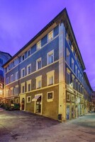 Un edificio a più piani con uno stile architettonico classico, caratterizzato da un ingresso centrale con tenda e una serie di finestre su ogni piano.
