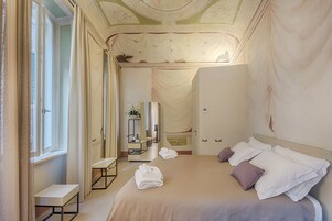 Una camera d'albergo con un letto grande, un comodino, uno specchio e una finestra con tende.