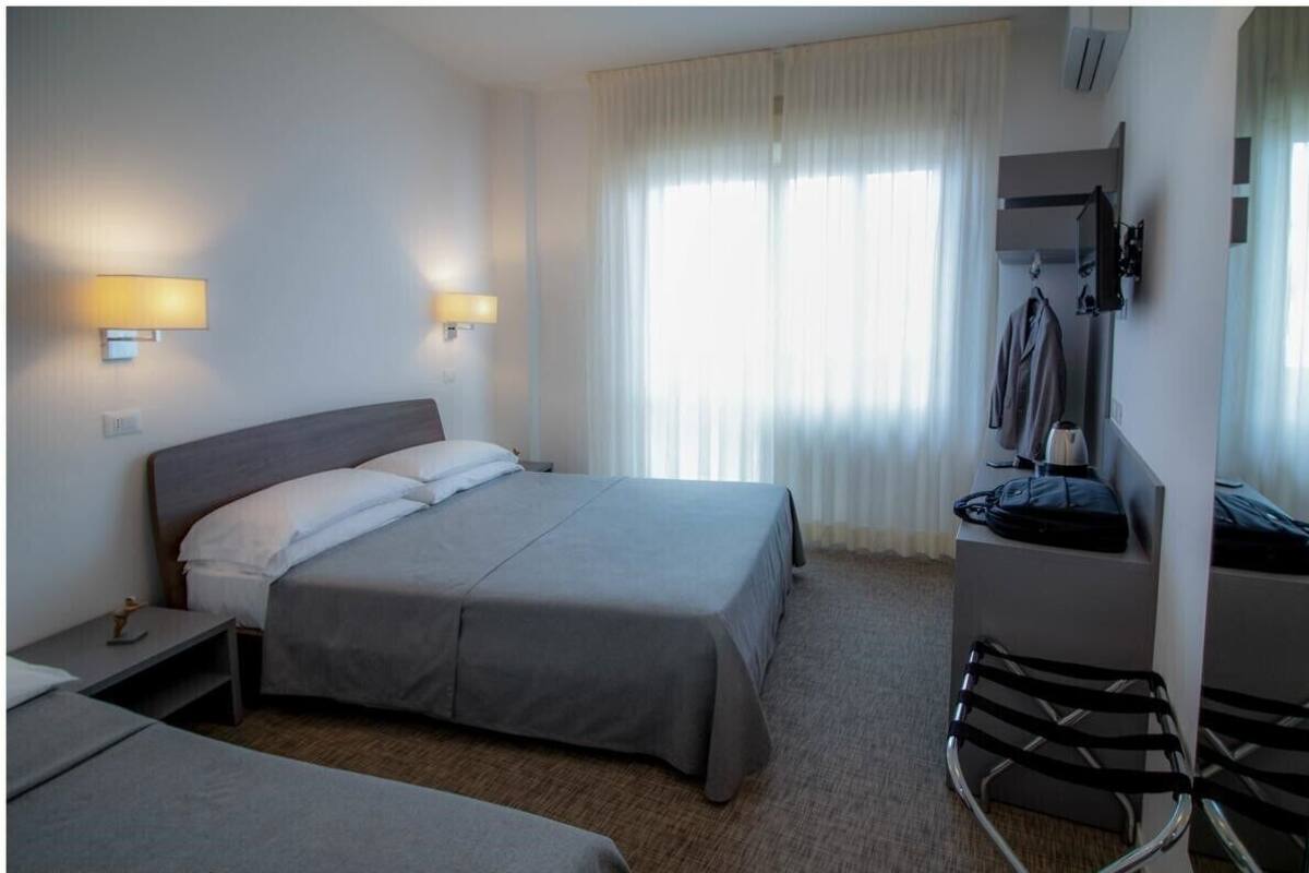 A hotel room with a bed, bedside tables, a chair, a wardrobe, and a window with curtains.